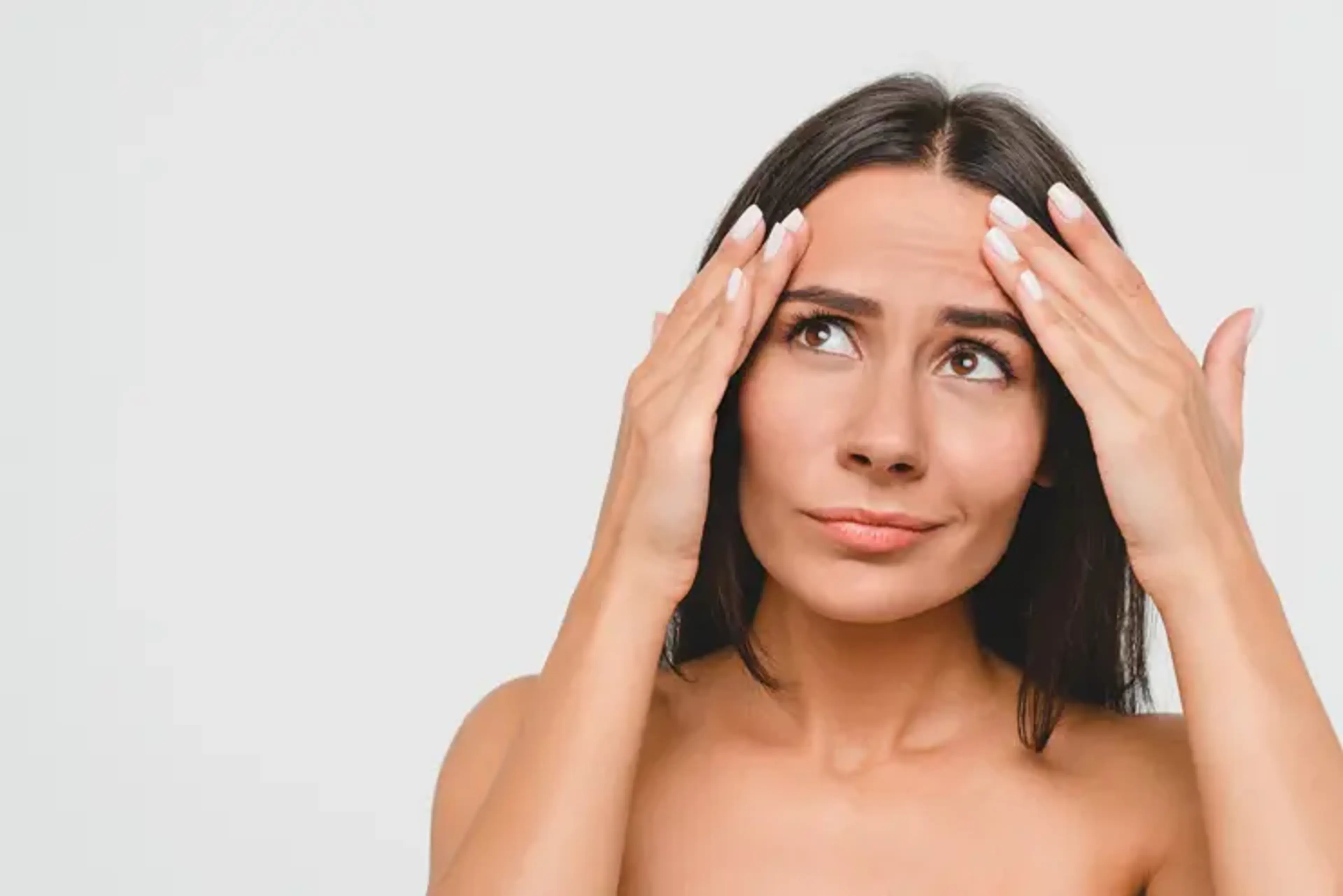 Woman examining forehead lines and early signs of wrinkles, expressing concern about aging skin and the need for wrinkle-reduction treatments.