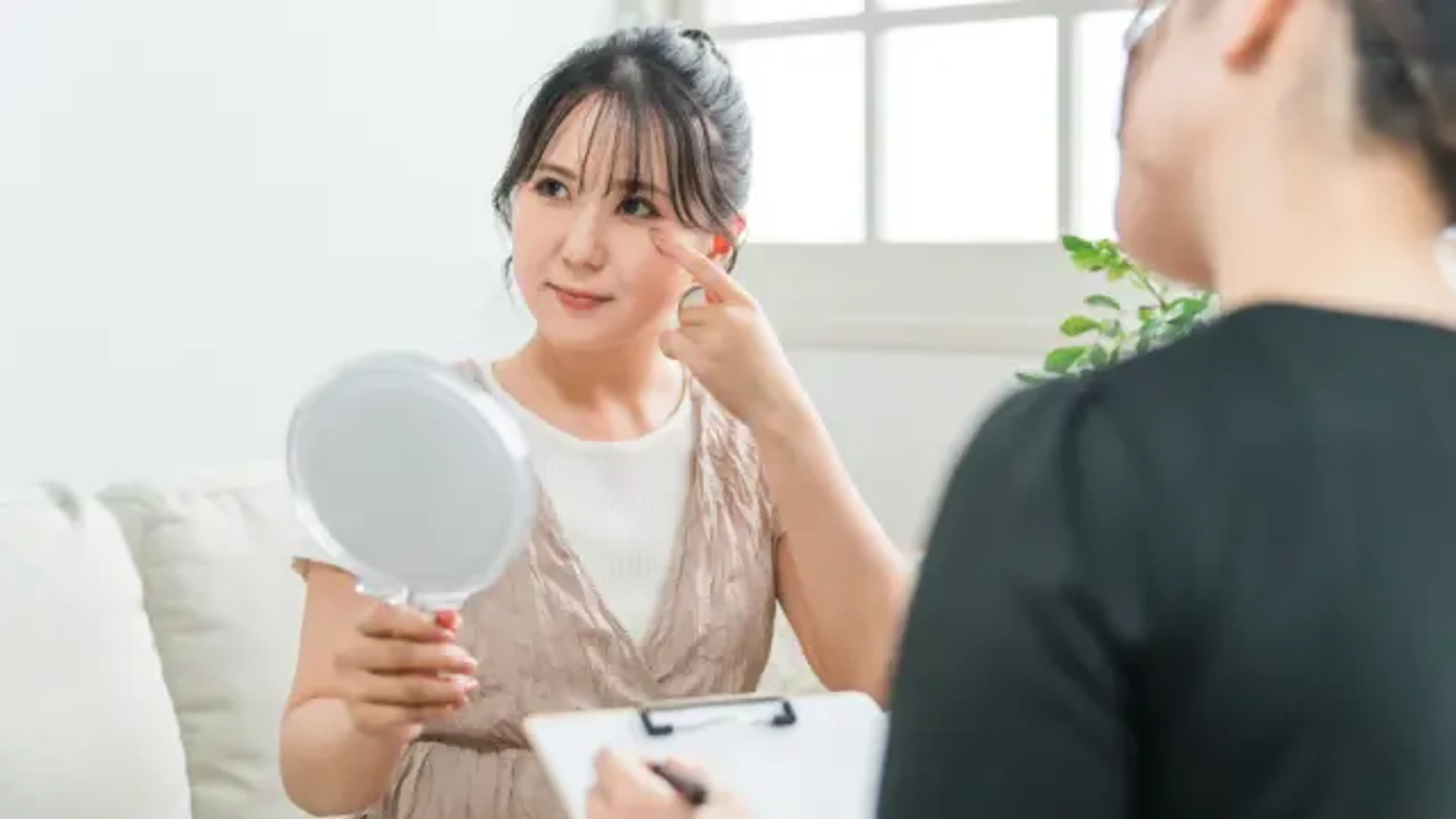 Patient pointing to eyelid area during consultation for double eyelid surgery with mirror assessment