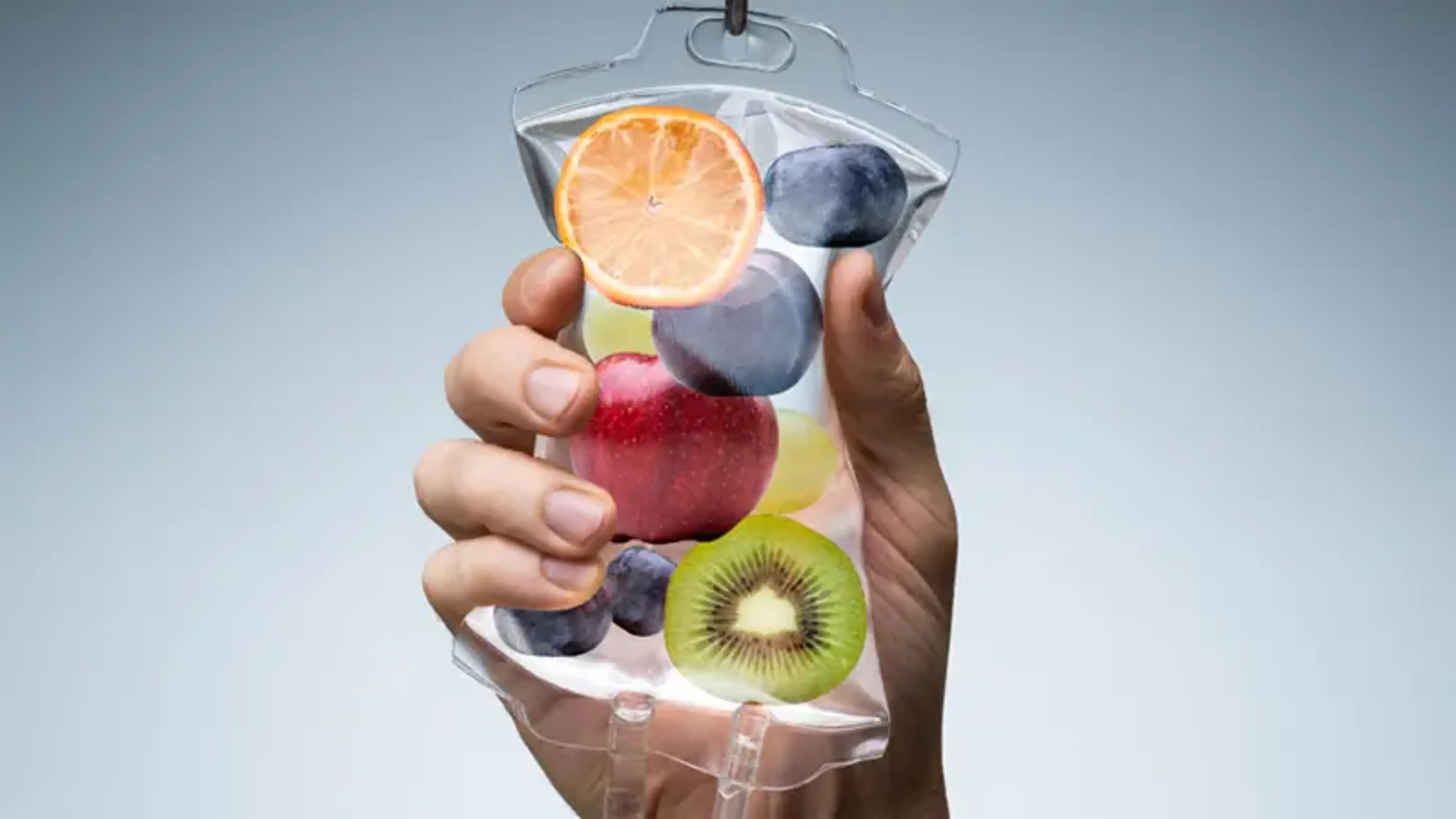 Hand holding a transparent IV fluid bag filled with colorful fruits, symbolizing nutrient-rich IV therapy and vitamin infusion treatments for enhanced hydration and wellness.