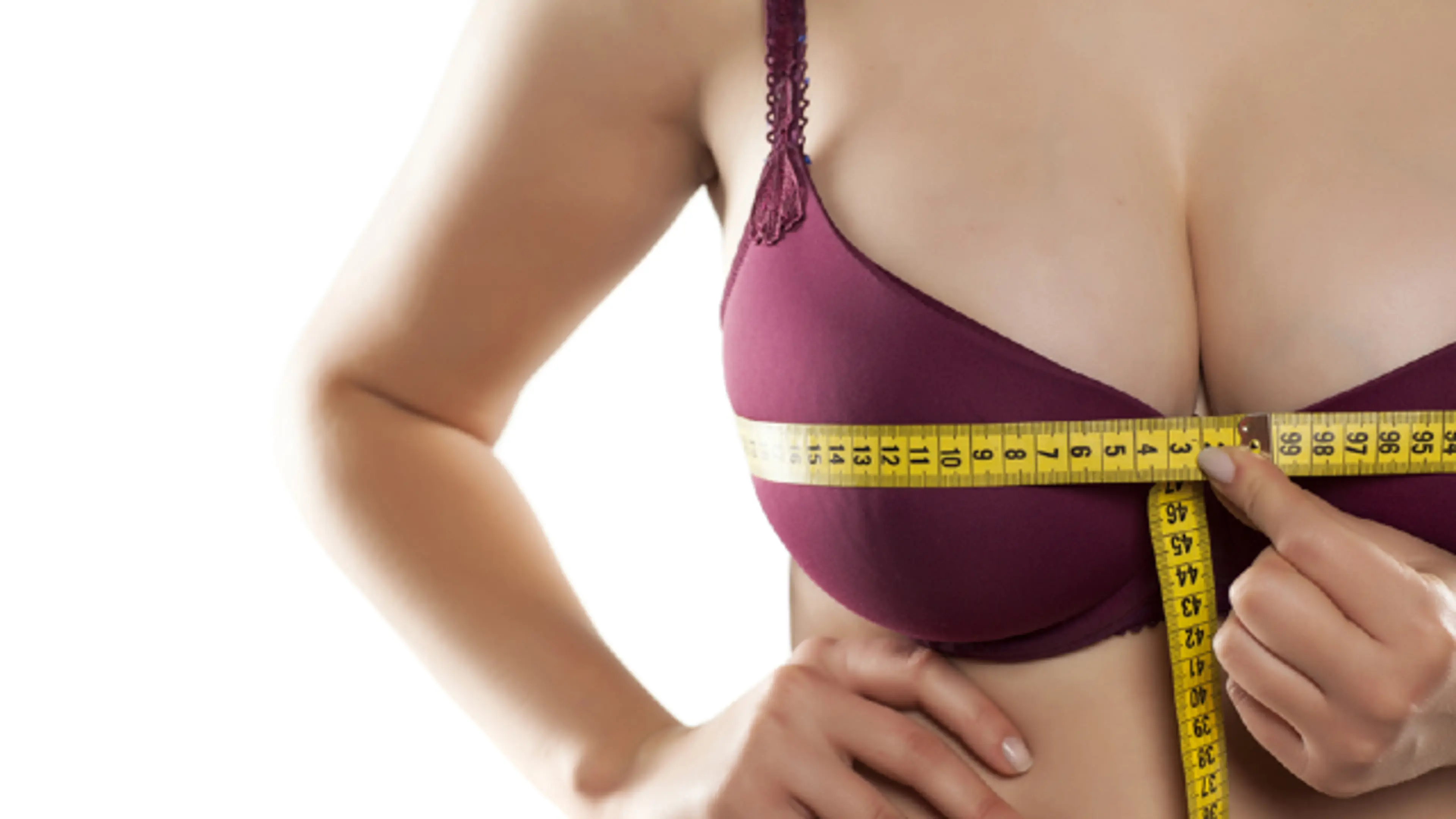 Woman measuring bust size with a tape measure while wearing a bra
