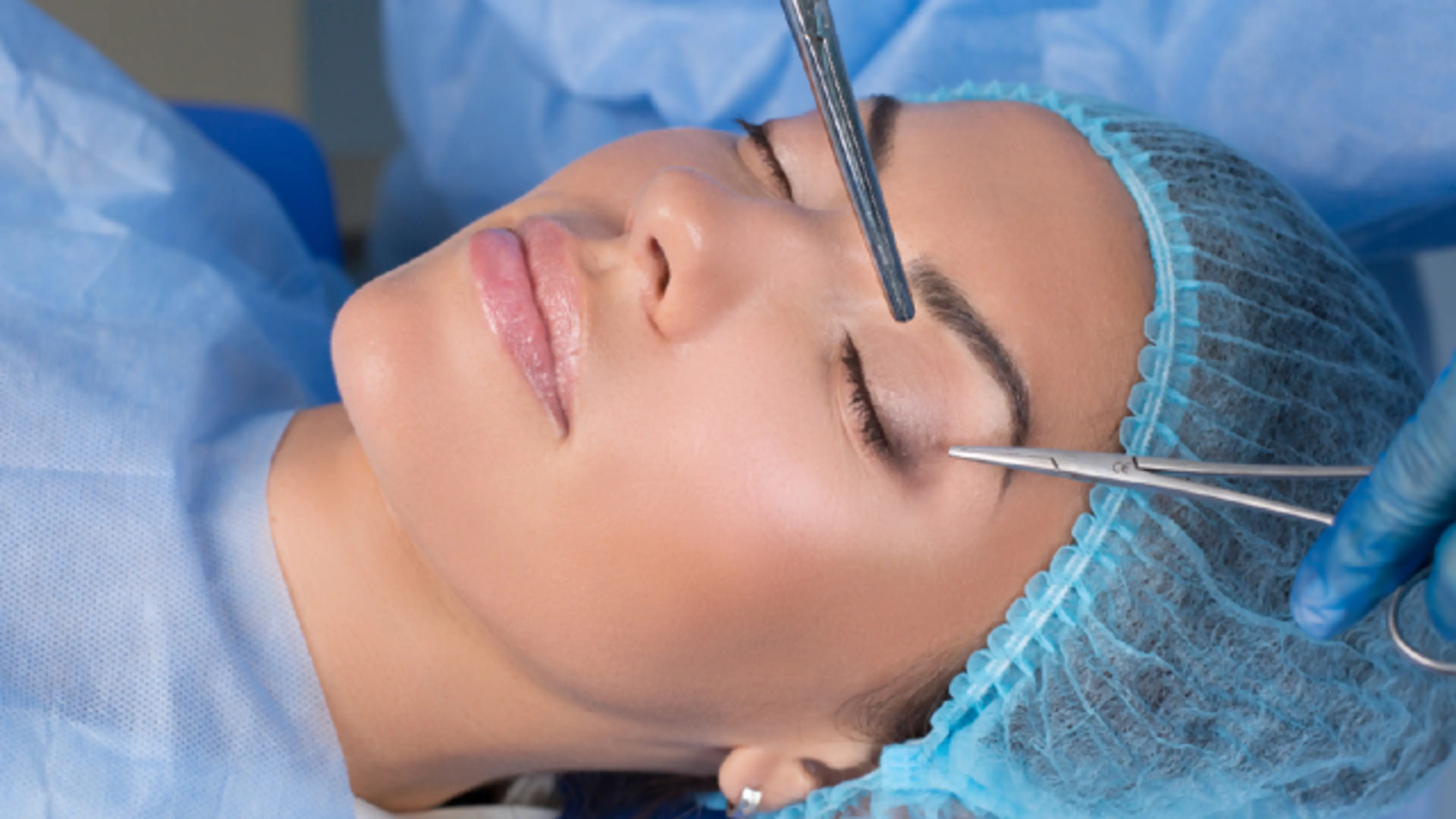 Patient undergoing eyelid surgery with surgical instruments in clinic setting