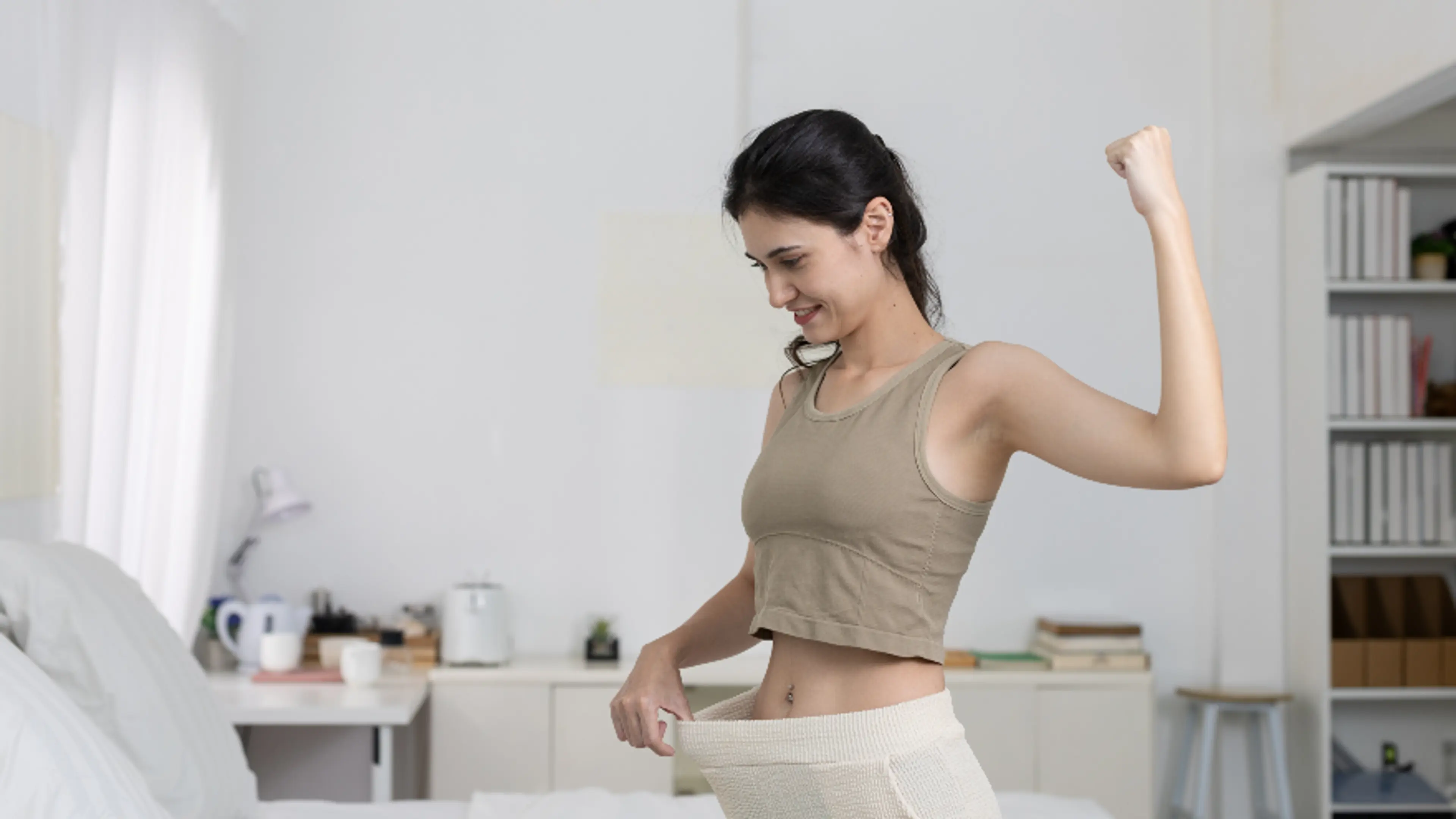 Người phụ nữ ăn mừng giảm cân, cầm phần thắt lưng rộng cho thấy sự biến đổi cơ thể