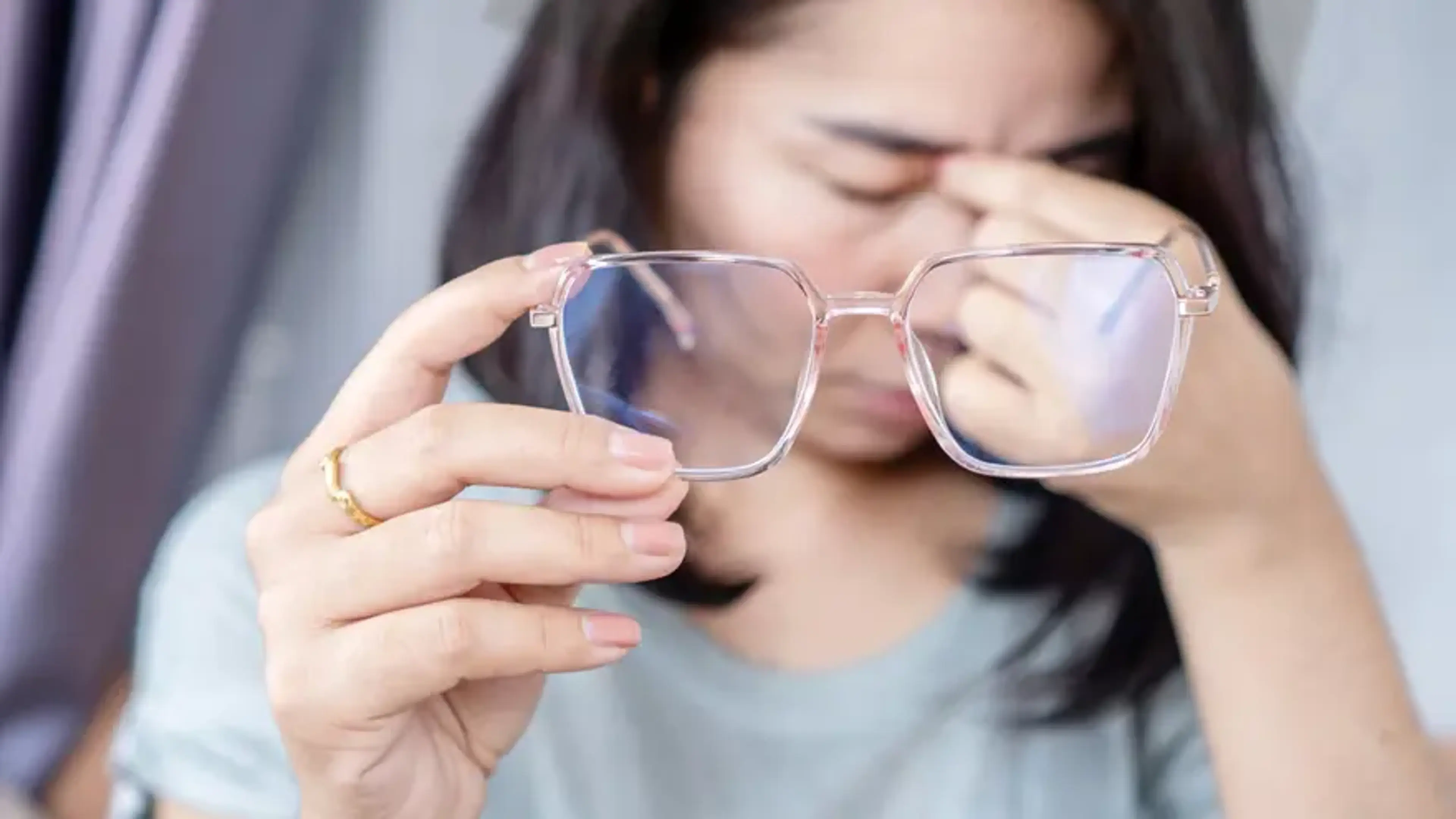 Person holding eyeglasses and rubbing eyes, showing blurred vision and eye strain caused by astigmatism