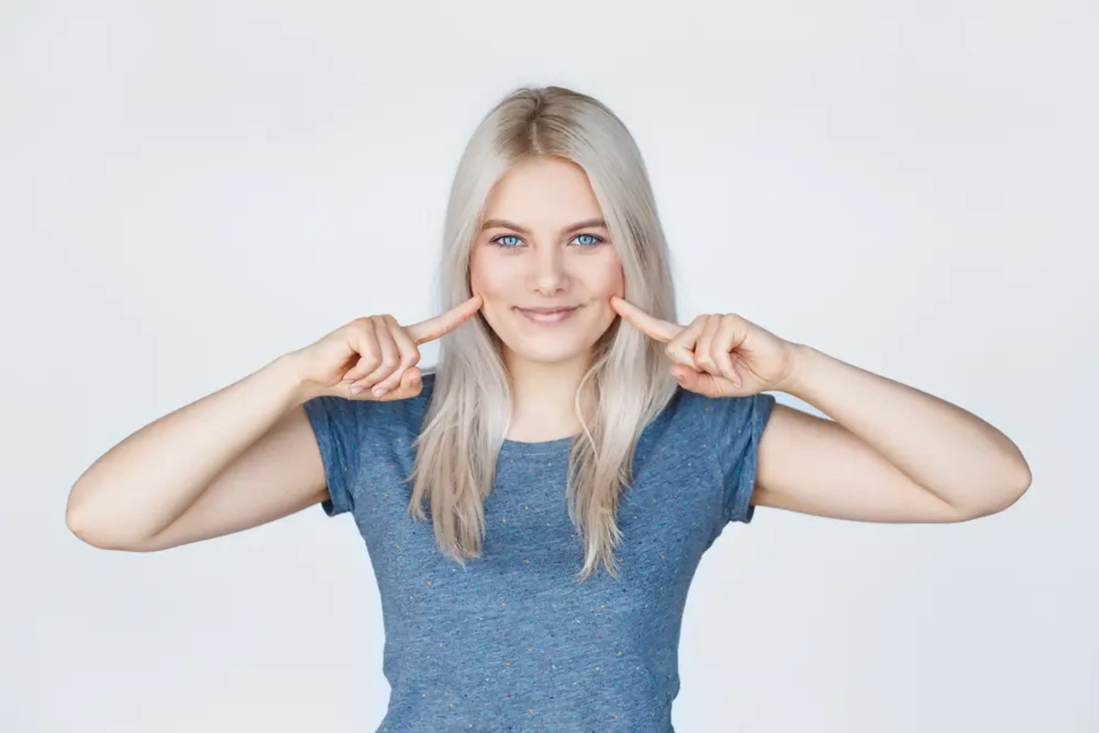Woman pointing to cheek dimples representing dimple removal surgery for smoother and more uniform facial contour